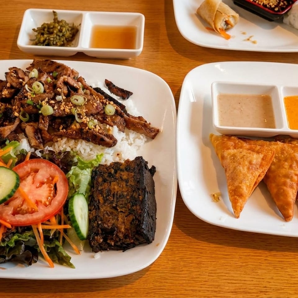 Plates of Vietnamese food, including grilled pork with rice, salad, and fried dumplings with dipping sauces.