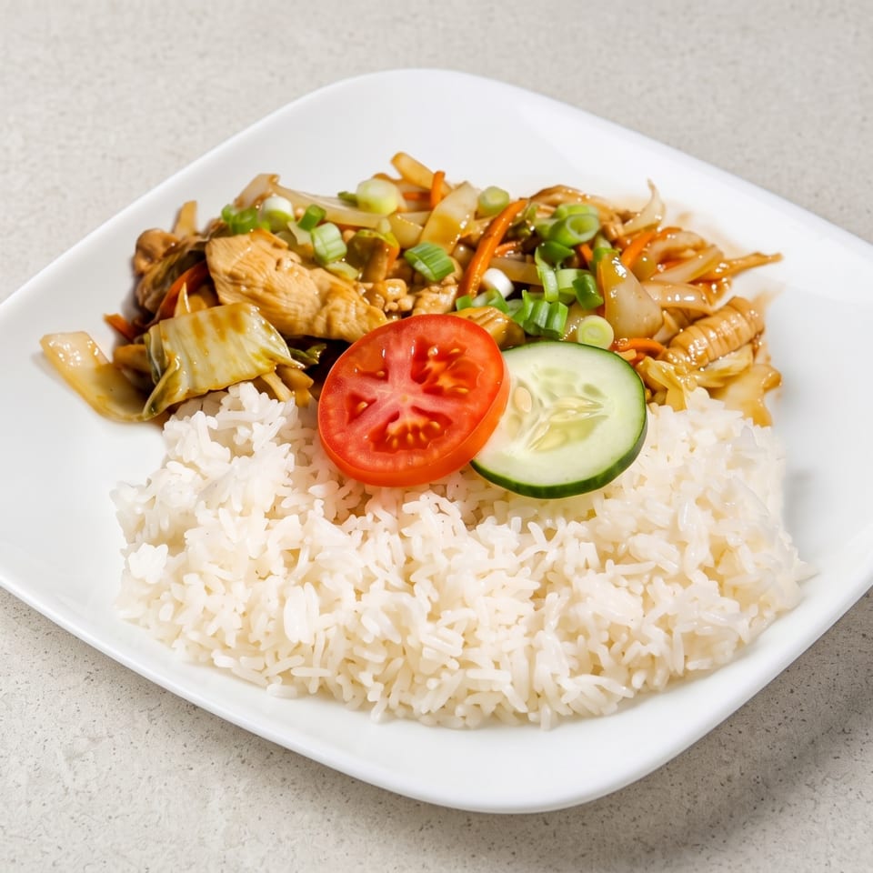 Chicken stir-fry with vegetables and white rice, garnished with tomato and cucumber slices.