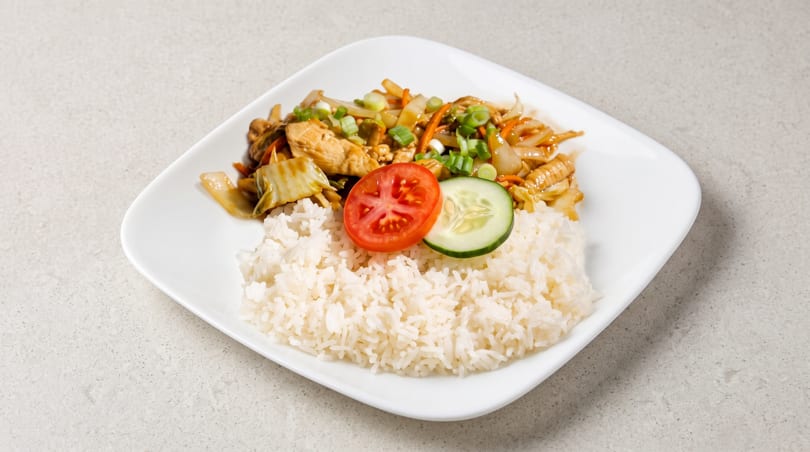 Chicken stir-fry with vegetables and white rice, garnished with tomato and cucumber slices.
